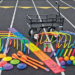 Colorful athletics training equipment arranged on a running track, including mini hurdles, cones, balls, batons, and a utility cart.